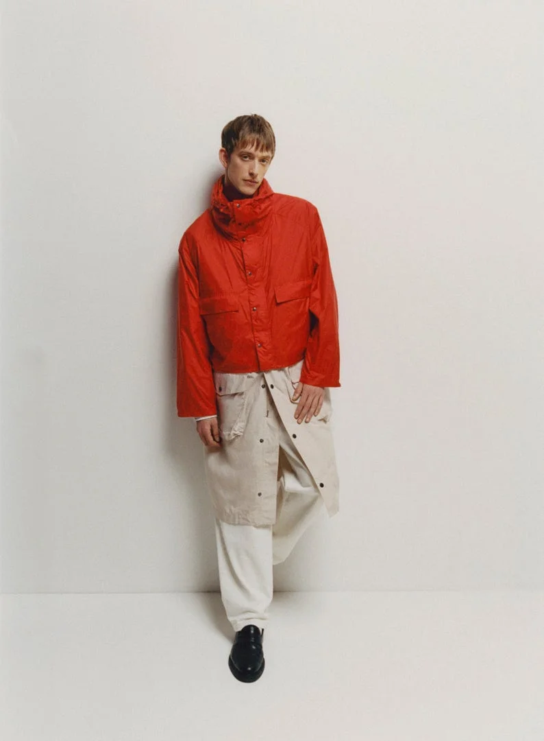 赤いショート丈ジャケットとベージュのスカート風アイテムを着用した男性