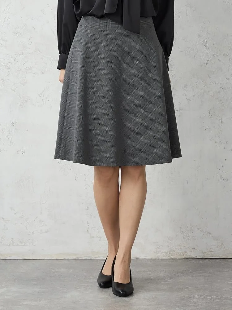 黒いブラウスとグレーのチェック柄Aラインスカート、黒いパンプスを着用した女性のファッション写真。