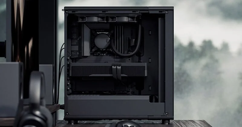 黒いPCケースの内部が写されており、グラフィックボードやCPUクーラーなどの主要コンポーネントが確認できる。背景には霧のかかった森がぼんやりと見える。全体的にモノトーンで統一されたモダンな印象の画像である。