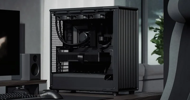 黒いモダンなデスクトップPCのセットアップが写っています。内部が見えるPCケースにはグラフィックカードや水冷クーラーが搭載され、モニター、スピーカー、キーボード、マウスがデスクに配置されています。