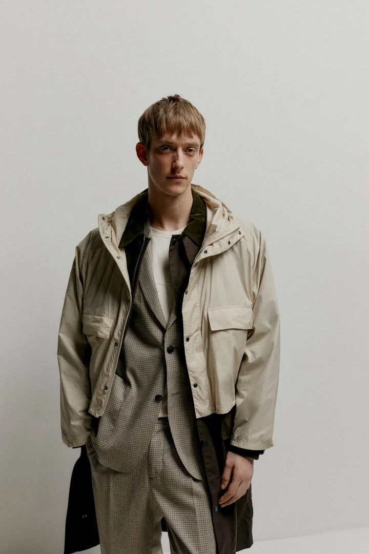 ベージュのフード付きジャケットとチェック柄のスーツをレイヤードした男性